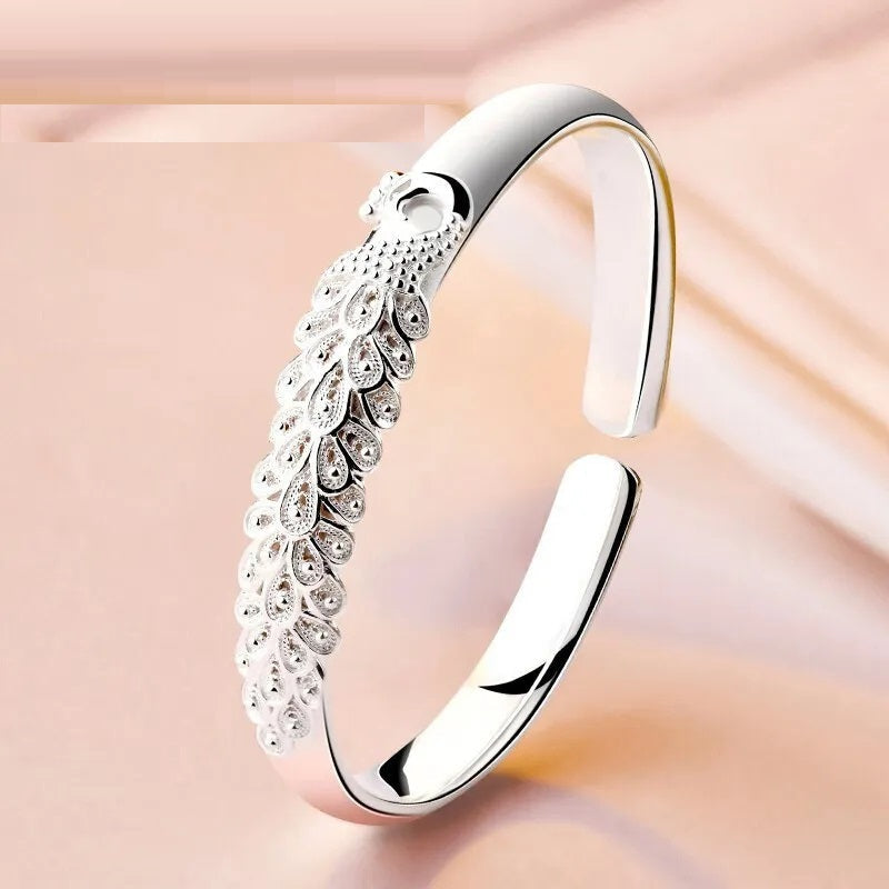 Nahaufnahme eines eleganten Damen-Silberarmbands mit schillerndem Pfau, feiner Tier-Schmuck.