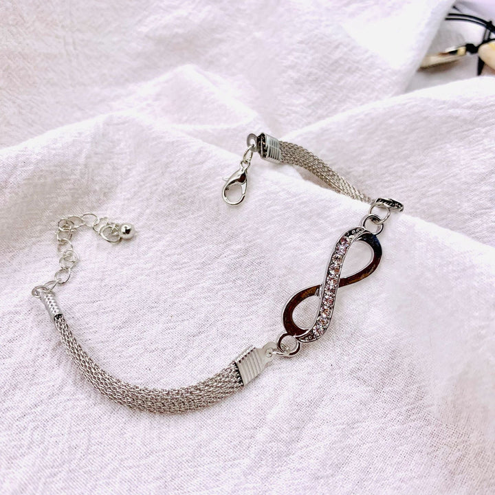Damenhand trägt ein filigranes Silber-Infinity-Armband, Ausdruck von Eleganz und Zuneigung.