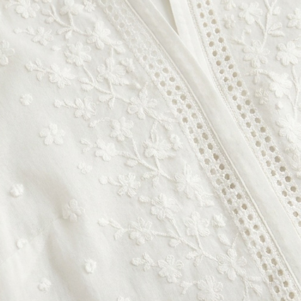 Weiße Damenbluse mit floral bestickten Ärmeln und Manschetten, elegante Knopfleiste.