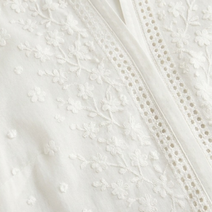 Weiße Damenbluse mit floral bestickten Ärmeln und Manschetten, elegante Knopfleiste.