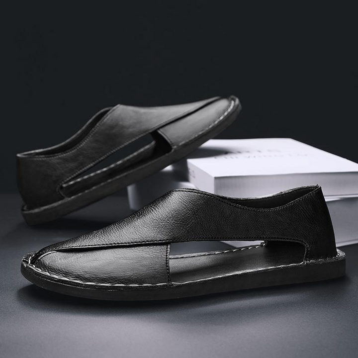 Seitliche Ansicht der Herren Slipper mit Ausschnitten. Zeigt die flache Sohle und das bequeme Slip-On Design.