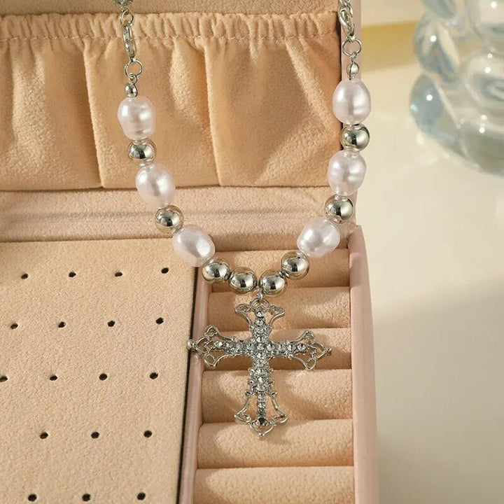 Nahaufnahme des Perlenkreuz-Anhängers einer Damenhalskette. Feine Perlen auf poliertem Silber. Klassische Eleganz.