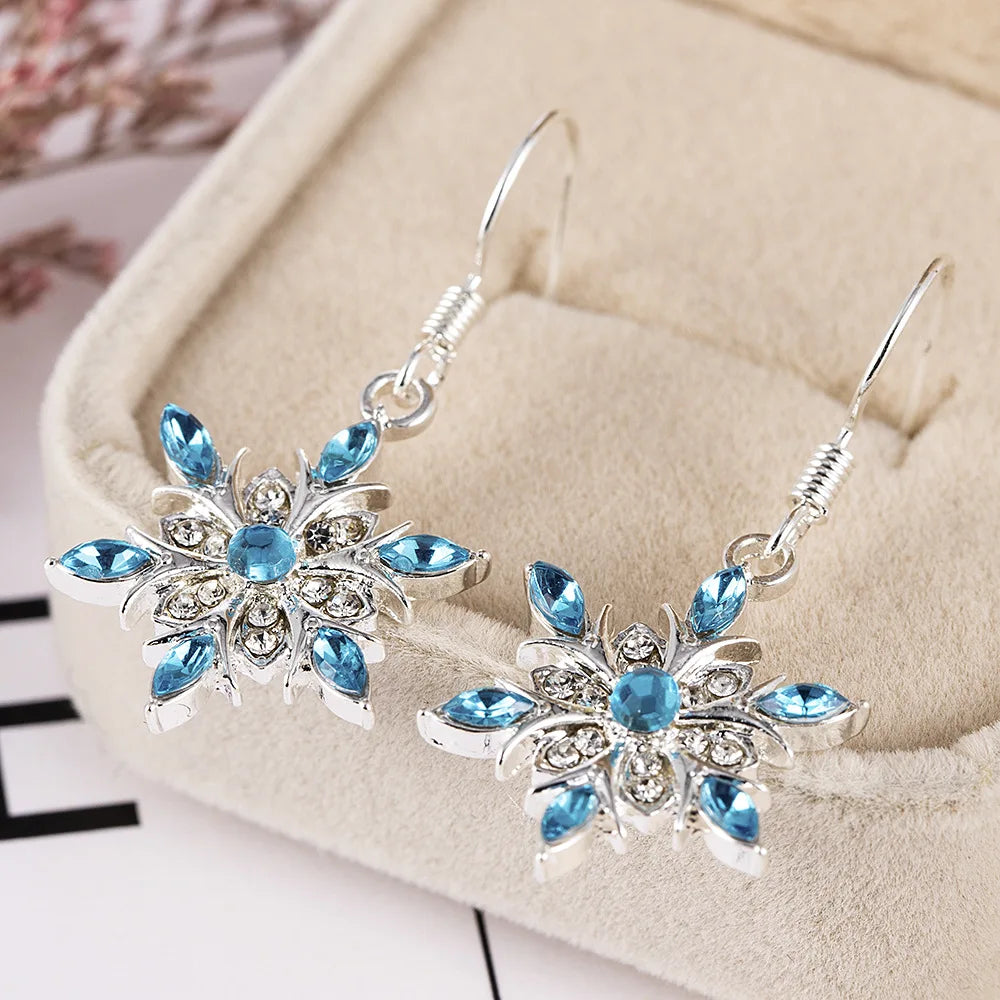 Funkelnde Schneeflocken-Ohrringe für Damen mit blauen Strasssteinen. Festlicher Schmuck als Geschenkidee.
