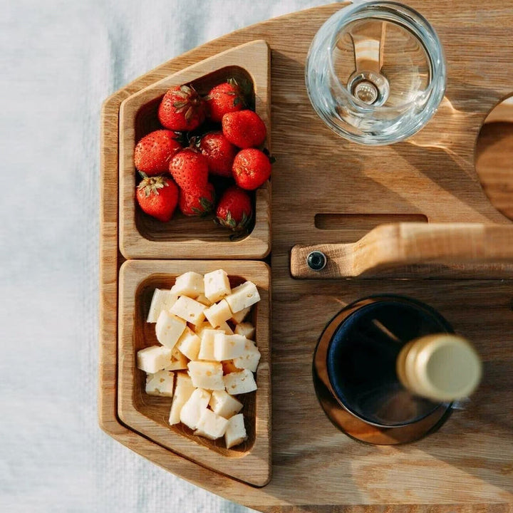 Tragbarer Holz-Picknicktisch mit zwei Weingläsern und einer Flasche Rotwein, bereit für den Garten.