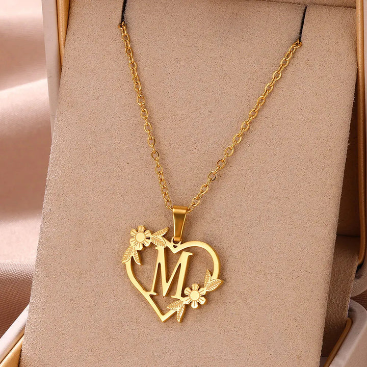 Nahaufnahme: Goldfarbene Damen Halskette, filigraner Initialen-Anhänger mit floralem Herz, eleganter Edelstahl-Schmuck.