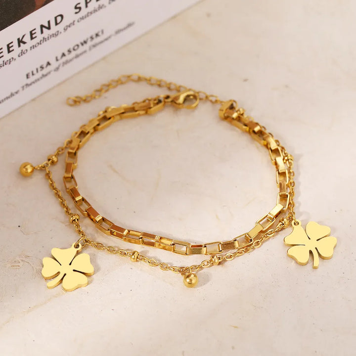 Modernes Damenarmband mit Kleeblatt-Charme, in Gold und Silber, elegant am Handgelenk getragen.