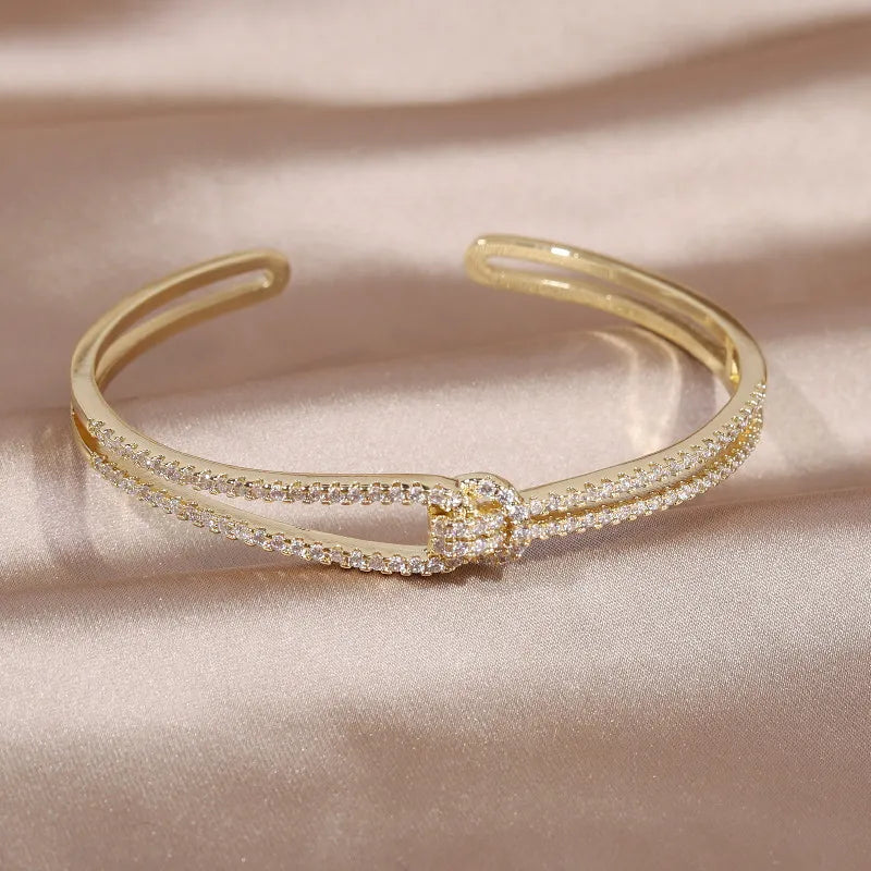 Damen Kristallarmreifen: zeitloses Design mit glänzenden Steinen und einem goldenen Knoten.