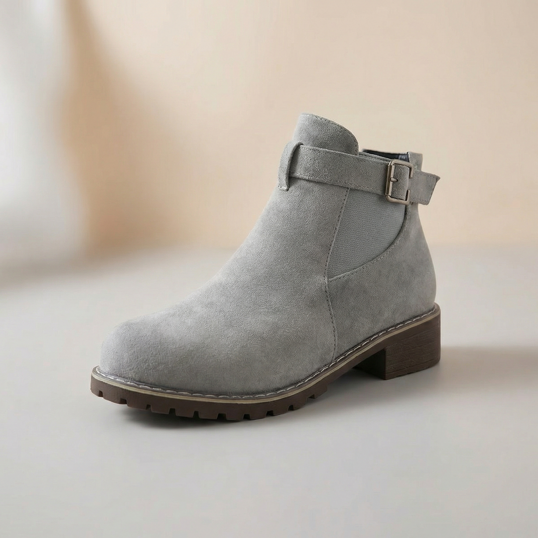 Seitenansicht: Grau-braune Damen Stiefeletten aus Wildleder-Optik, mit verstellbarer Schnalle & niedrigem Blockabsatz.