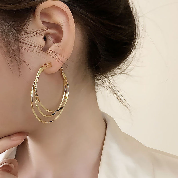 Dame präsentiert elegante goldfarbene Dreifach Hoop Ohrringe mit Funkelsteinen. Zeitloses Accessoire für den Abend.