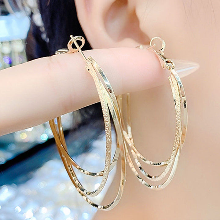 Nahaufnahme: Funkelnde Steine auf luxuriösen dreifachen Hoop Ohrringen für Damen. Edler Goldschmuck-Akzent.