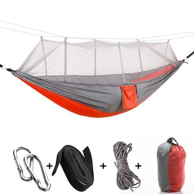 Aufgehängte Camping-Hängematte mit Mückennetz zwischen Bäumen im Wald, bereit für die Nacht.