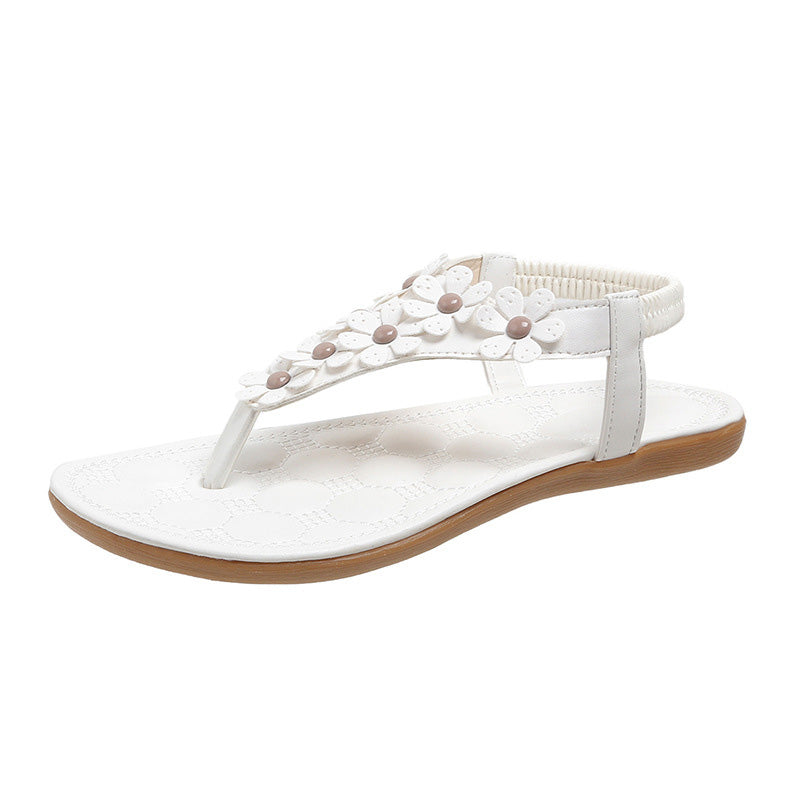 Detailaufnahme der blüten- & perlenbesetzten T-Steg Sandalen in elegantem Weiß für Damen.