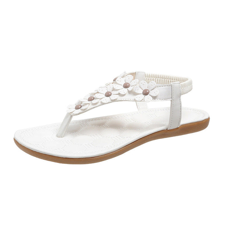 Detailaufnahme der blüten- & perlenbesetzten T-Steg Sandalen in elegantem Weiß für Damen.