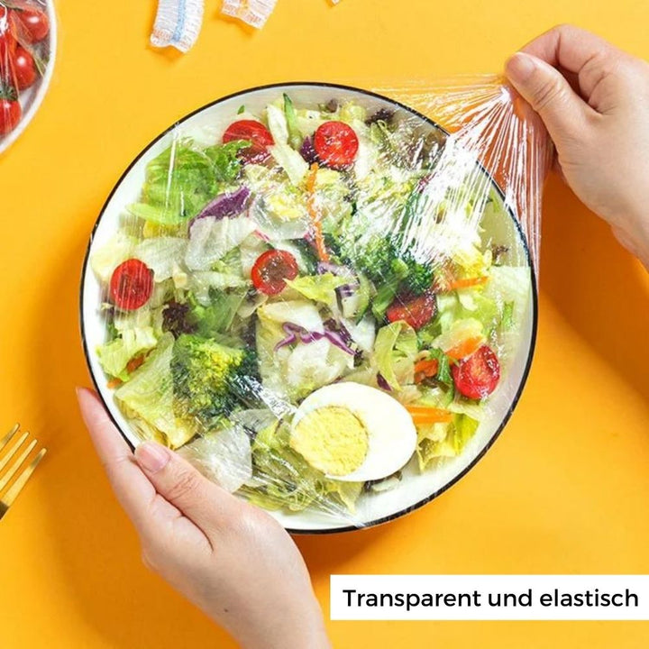 Eine Hand bedeckt eine Schüssel mit dehnbarem Frischhaltebeutel. Praktische, wiederverwendbare Abdeckhauben für Lebensmittel.